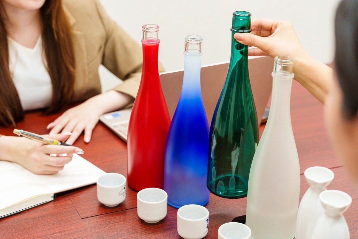 色とりどりのボトルと盃を囲んで商品設計を話し合う様子
